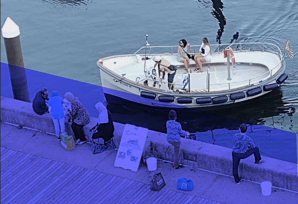 A group of people sitting on the waterfront near Pier 5, with a small boat docked nearby.